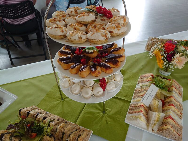 A tiered cake stand of meringues, tarts and finger sandwiches on a green table runner