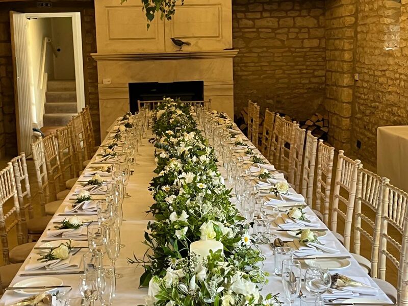 A long table in a stone barn, laid with white linen and a running garland of white flowers