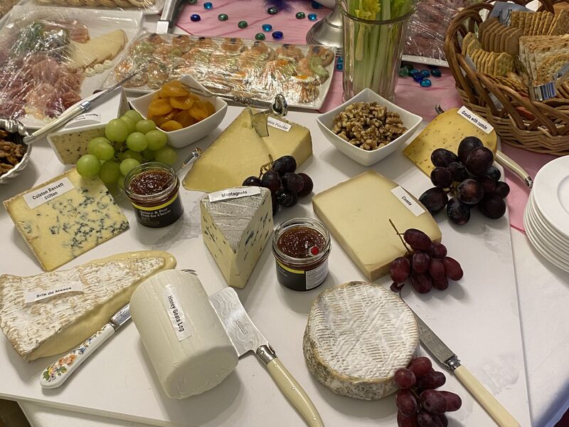 A cheeseboard with grapes, chutneys, crackers and butter on a dressed table