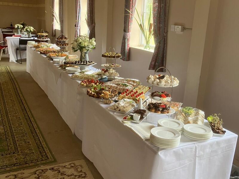 A long white buffet table beneath bunting in a village hall with a patterned rug