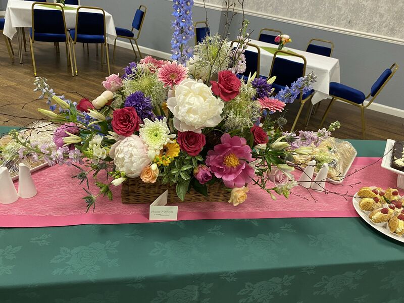 A low arrangement of peonies, roses and delphiniums in a basket along a buffet table